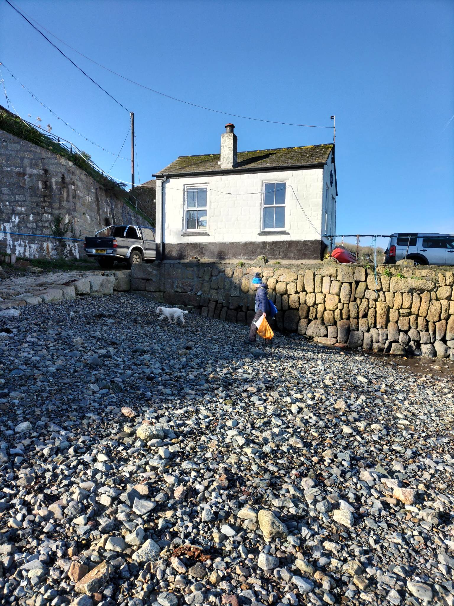 A building - Fisherman's Rest cafe - in the background, with beach cleaning on a pebbled beach in the foreground.